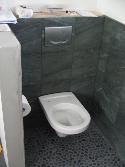 The toilet is in place, but is awaiting a seat. The dual flush control is also installed.